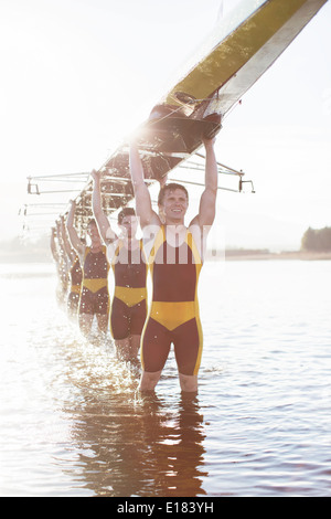 Il team di canottaggio che trasportano scull overhead a lago Foto Stock