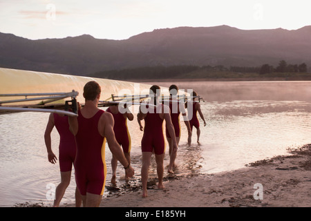 Il team di canottaggio che trasportano scull nel lago all'alba Foto Stock