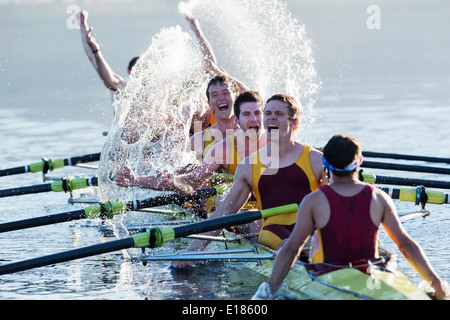 Il team di canottaggio schizzi e celebrando in scull sul lago Foto Stock