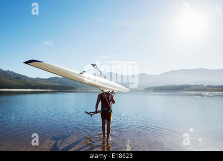 Uomo che porta il canottaggio scull nel lago Foto Stock