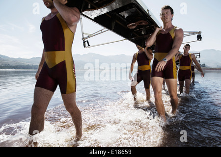 Il team di canottaggio che trasportano scull fuori del lago Foto Stock