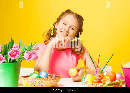 Ragazza sorridente si siede a tavola con le uova di Pasqua Foto Stock