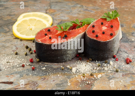 Closeup foto orizzontale di rosso fresco filetti di salmone, corso di spezie, erbe e le fette di limone con pietra naturale al di sotto di ardesia Foto Stock