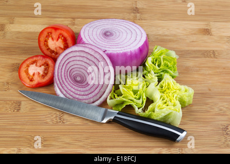 Ingrandimento orizzontale della foto appena cipolla rossa affettata, lattuga e pomodoro con coltello da cucina nella parte anteriore e di bamboo naturale il legno Foto Stock