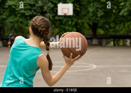 Giovani esili ragazza adolescente giocare a basket lancia la palla, vista da dietro Foto Stock