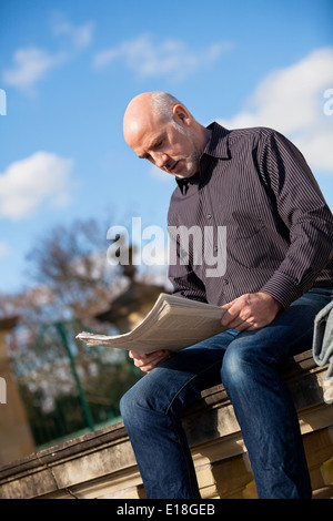 Uomo seduto sui gradini leggendo un giornale Foto Stock