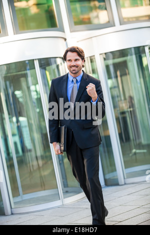 Motivati bel giovane imprenditore di lasciare il suo ufficio edificio con una valigetta sotto il suo braccio punzonatura il pugno in aria un Foto Stock