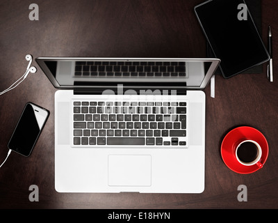 Macbook Apple computer portatile, iPhone Kindle tablet e una tazza di caffè sulla scrivania. Angolo di Alta Vista. Foto Stock