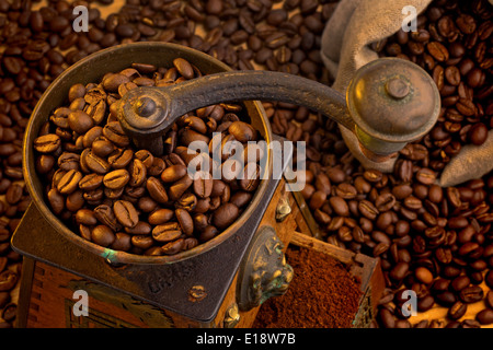 Viele Kaffeebohnen liegen neben einer Kaffeemühle. Frisch gemahlener Kaffee Foto Stock
