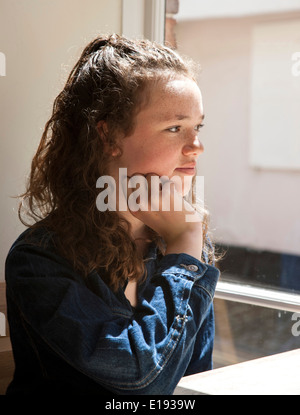 Giovane ragazza adolescente pensare guardando attraverso la finestra Foto Stock