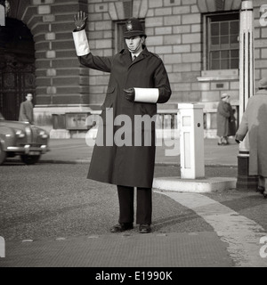 1960s. Foto storiche di un poliziotto britannico indossa un casco, cape e maniche bianco traffico di segnalazione in una strada di Londra Foto Stock