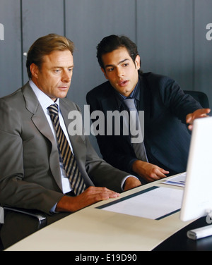 Due uomini di affari concentrati a lavorare insieme su un computer portatile in ufficio Foto Stock