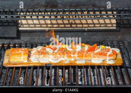 Cucinare il salmone in legno di cedro in barbecue, guarnito con cipolle, pomodori, aneto e condimenti a base di erbe Foto Stock