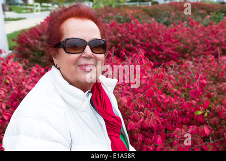 Senior lady godendo l'autunno intorno cespugli di masterizzazione Foto Stock