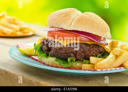 Una deliziosa grigliata di cheeseburger e patatine fritte in un picnic esterno barbecue impostazione. Foto Stock