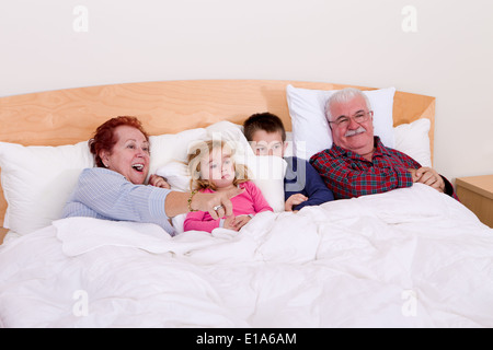 Nonni guardando la TV nel letto con loro grand kids, sembrano entusiasti, forse il suo un film d'avventura Foto Stock