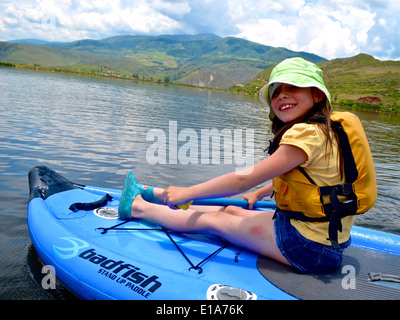 Una ragazza si siede sul suo Stand Up Paddleboard mentre fuori ad esplorare i laghi vicino a Cusco, Perù Foto Stock