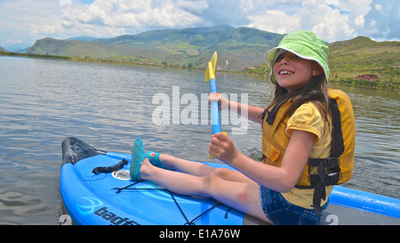 Una ragazza si siede sul suo Stand Up Paddleboard mentre fuori ad esplorare i laghi vicino a Cusco, Perù Foto Stock