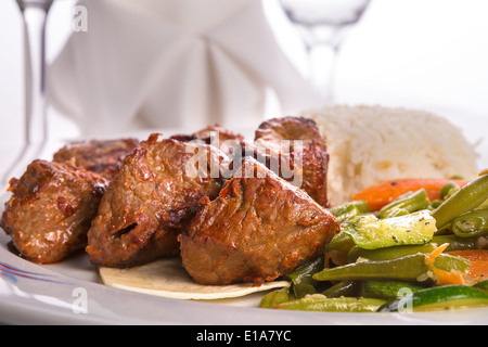 Macro shot di shish kebab guarnito con verdure e riso pilaf, igienico e vetro di vite sullo sfondo Foto Stock