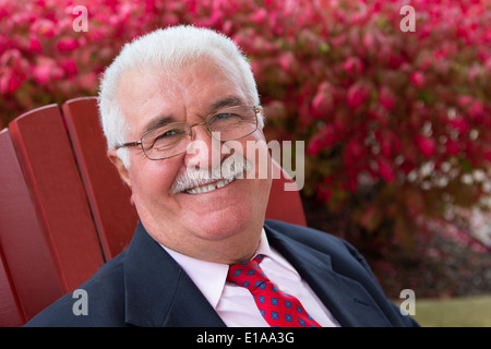 I capelli bianchi imprenditore senior al di fuori su una sedia rossa sorridente grande a voi Foto Stock