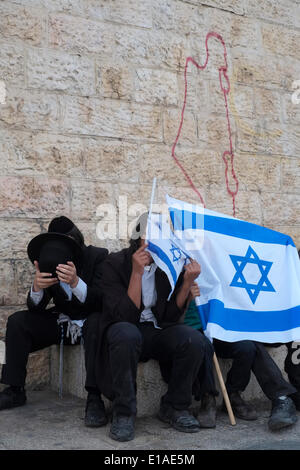 Gerusalemme, Israele. 28 Maggio, 2014. Gli ebrei ortodossi di nascondersi dietro la bandiera israeliana con graffiti nella parete raffiguranti lo stato di Israele nella città vecchia nel corso del XLVII anniversario di Gerusalemme la riunificazione il 28 maggio 2014. Israele ha segnato il suo quarantasettesimo Gerusalemme giorno commemorativo della riunificazione della città in seguito th 1967 Guerra di sei giorni dalla tradizionale giorno Gerusalemme bandiera marzo attorno alla città vecchia, come pure diverse cerimonie. Credito: Eddie Gerald/Alamy Live News Foto Stock