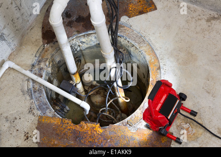 La riparazione di una pompa in un seminterrato con una spia LED rossa illuminando la fossa e le tubazioni per il drenaggio di acqua di terra Foto Stock