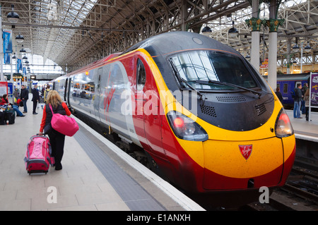 Signora a piedi passeggero sulla piattaforma con i bagagli alla Vergine treno pendolino a Manchester Piccadilly Station; donna con valigia rosa; bagagli Foto Stock