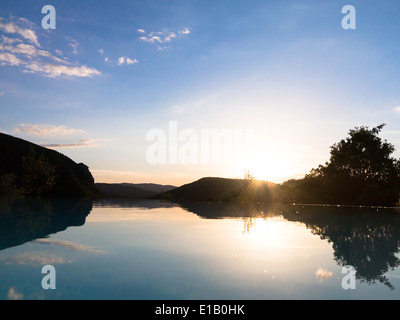 I trend con orizzonte di riferimento e riflessioni in una piscina infinity contro un Cielo di tramonto Foto Stock