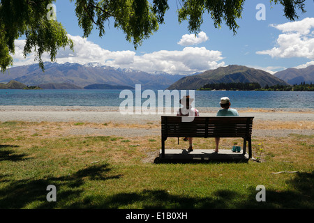 Coppia seduta sul banco in riva al lago, il lago Wanaka, Wanaka, Otago, Isola del Sud, Nuova Zelanda e Sud Pacifico Foto Stock