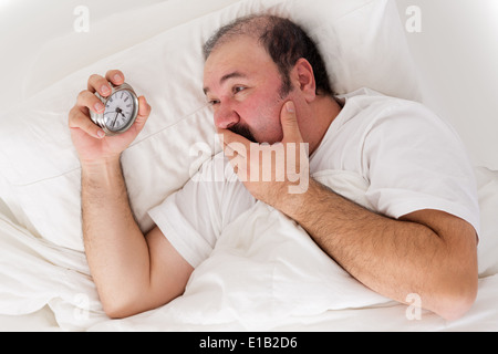 Uomo che soffrono di insonnia cercando di dormire controllando il tempo per la sua sveglia nella disperazione come egli si rende conto che egli non si riattiva Foto Stock