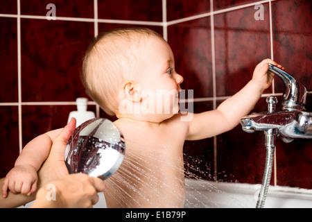 Carino il bambino gioca con rubinetto di acqua in bagno mentre a doccia Foto Stock