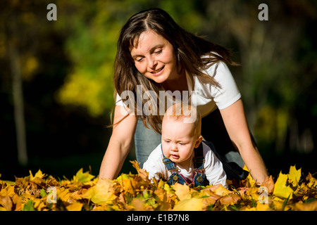 La madre gioca con il suo bambino in caduta foglie cadono sulla giornata di sole Foto Stock