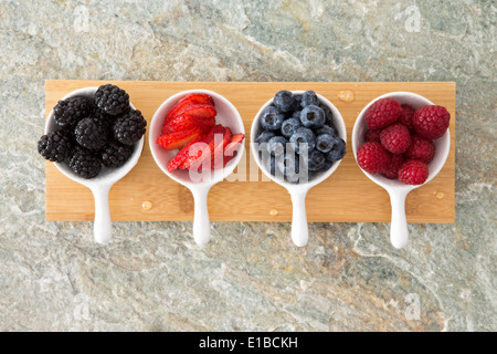 Un assortimento di frutti di bosco freschi in piatti di assaggiatori visto dal di sopra allineate sulla tavola di legno su una pietra bancone cucina con more Foto Stock