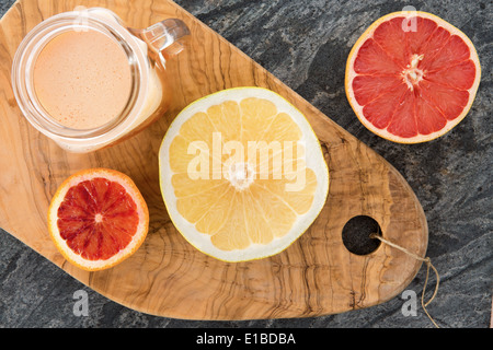 Preparata di fresco e succo di pompelmo con dimezzato ruby e pompelmo ordinario utilizzati come ingredienti in un vecchio olivewood tagliere Foto Stock