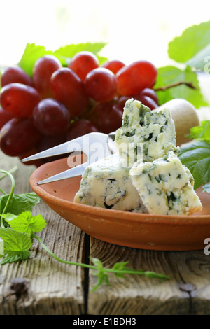 Pezzi di formaggio blu con uve rosse su un tavolo di legno Foto Stock