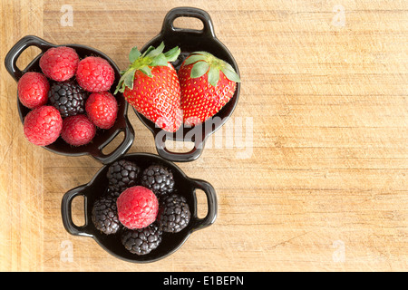 Vista aerea del tre ramekins ceramica piena di sani freschi maturi di frutti di bosco misti compresi fragole, more e raspbe Foto Stock