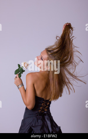 Pretty girl in abito nero con girare indietro tenendo una rosa bianca, studio isolato su sfondo scuro Foto Stock