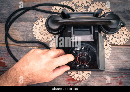 Uomo di effettuazione della chiamata sul telefono rotante di comporre i numeri con il suo dito ad alto angolo di visione dello strumento su un vecchio tavolo in legno Foto Stock