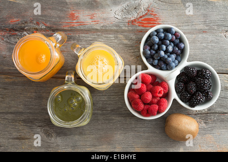 Succo di frutta fresca in tre caraffe in vetro con mango, arancio e kiwi blend servita su un vecchio rustico tavolo in legno con un piatto di Foto Stock