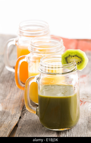 Il vasetto di vetro di sano frullato di kiwi guarnito con una fetta di kiwi freschi insieme con vasi di mango e il succo di arancia in una r Foto Stock