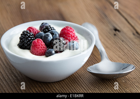 Ciotola di fresco di frutti di bosco misti e yogurt con fattoria fresco fragole, more e mirtilli servite su un tavolo di legno Foto Stock