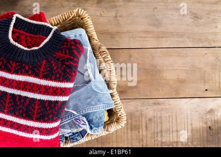 Lavanderia in vimini cesto pieno di freschi puliti lavati abbigliamento invernale visto dal tettuccio in piedi in un angolo sul legno rustico b Foto Stock