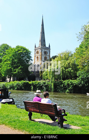 Chiesa della Santa Trinità si vede attraverso il fiume Avon con una coppia seduta su una panchina in primo piano, Stratford-Upon-Avon, Regno Unito. Foto Stock