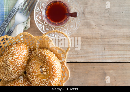 Vetro tradizionale tazza di tè turco e pane appena sfornato croccante crosta di sesamo bagel in un disegno decorativo cesto in vimini vista da sopra Foto Stock