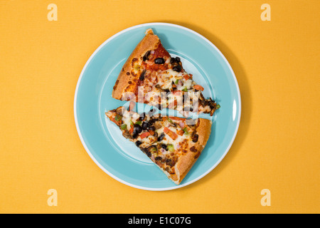 Vista aerea di due appena sfornato fette di pizza salato con formaggio, pomodori, olive ed erbe su una piastra blu su un giallo ba Foto Stock