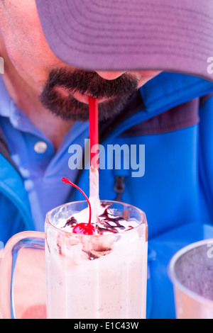 Uomo con un pizzetto barba flessione in avanti in un cappuccio di picco di bere un delizioso frullato cremoso condito con una ciliegia e cioccolato Foto Stock