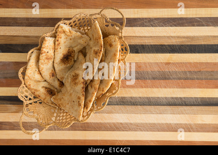 Deliziosi crostini di grano intero appartamento naan fette di pane, un pane lievitato cotto in un tandoor forno di argilla, servita in un cesto di vimini Foto Stock