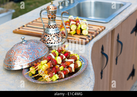 Bagno turco shish kebab con la carne e le verdure su una piastra di rame con abbinamento elegante brocca su un contatore in un dehor estivo Foto Stock