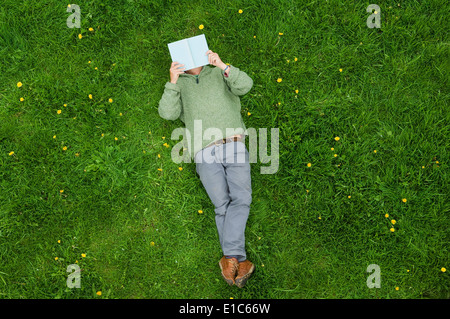 Un uomo disteso sulla sua schiena sull'erba, la lettura di un libro. Foto Stock