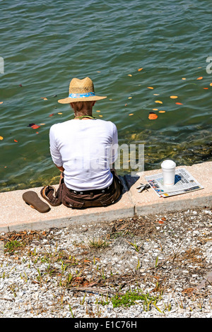 Una donna si siede sul lungomare e legge la sua carta, beve il suo caffè e gode di un momento solitario in Florida Foto Stock